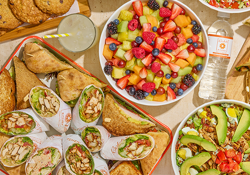 Catering spread with turkey wraps, chicken sandwiches, mixed berry fruit salad, and avocado cobb salad from Rachel's Kitchen