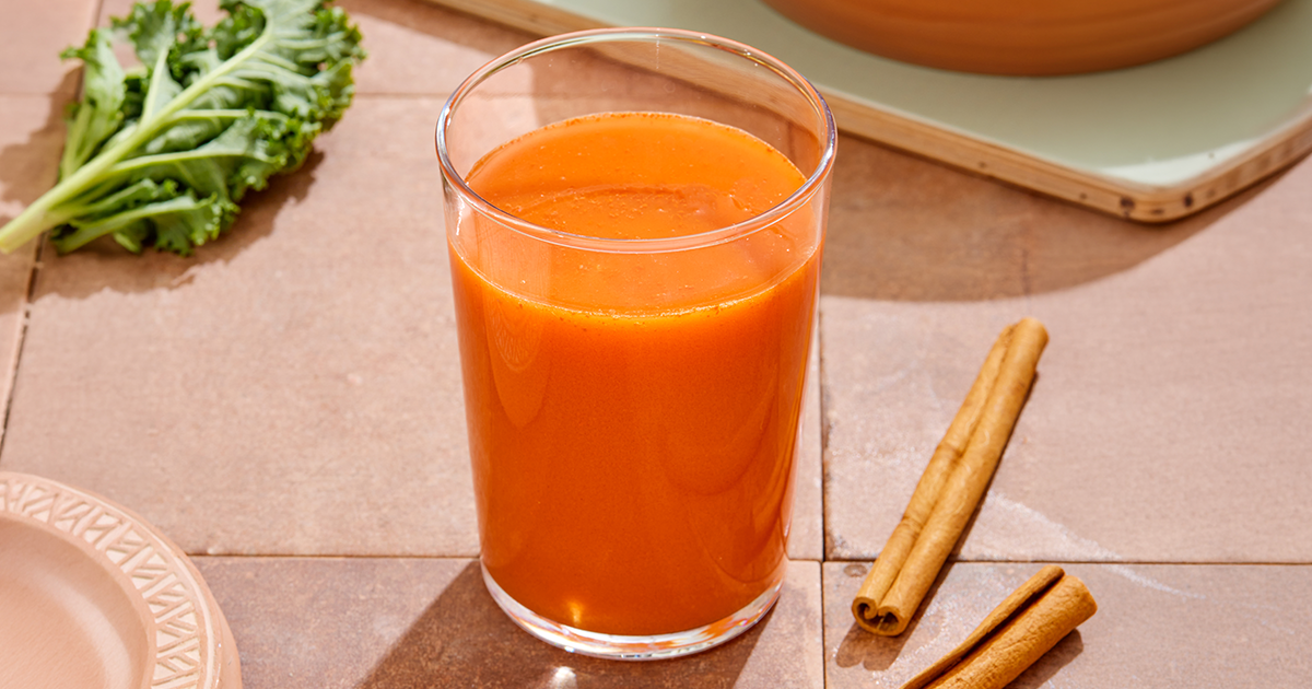 Glass of Rachel's Kitchen Apple Spice Juice with cinnamon sticks on the side
